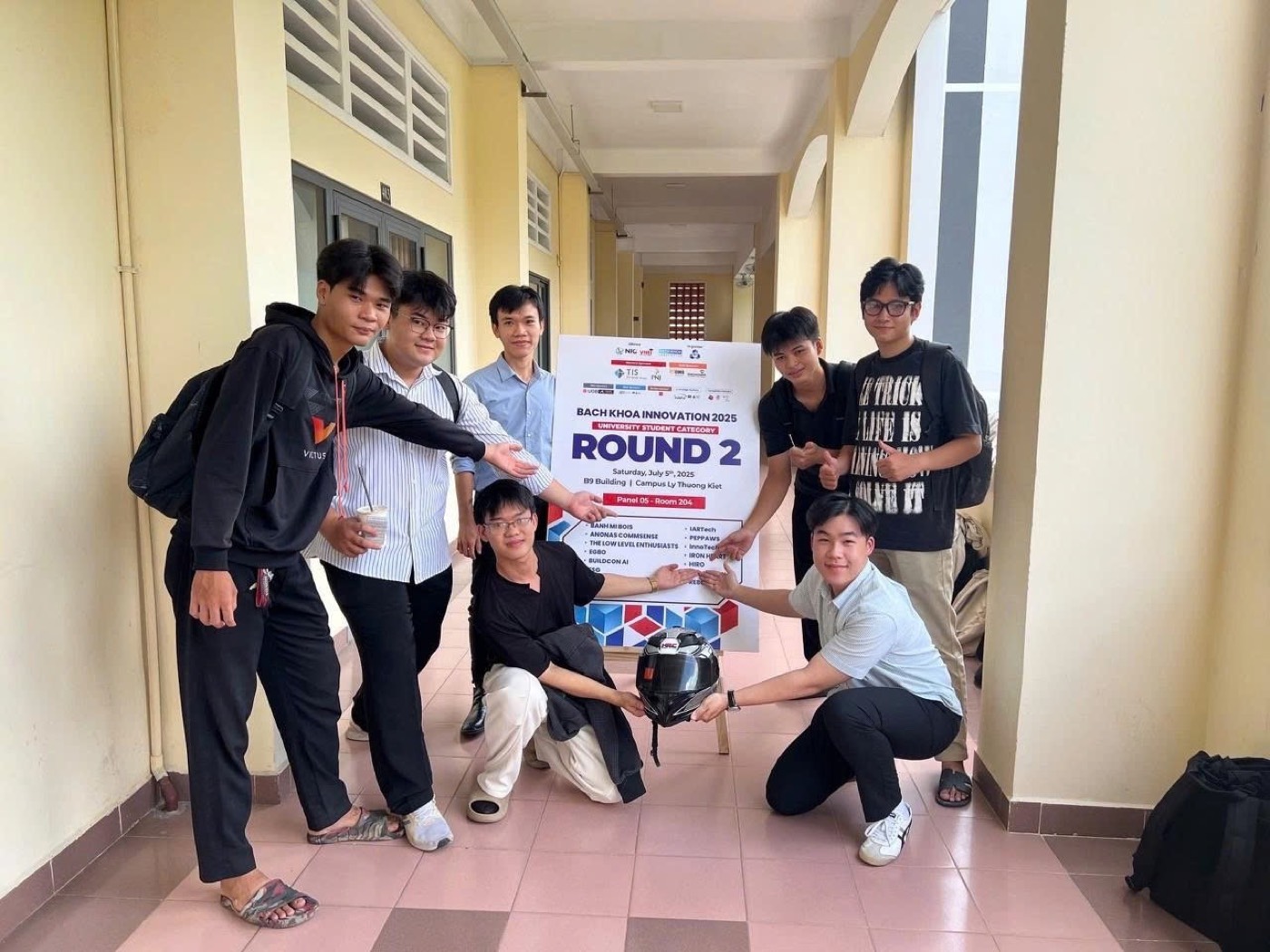 Team HIRO crouching around a motorcycle helmet beside the Bach Khoa Innovation 2025 round 2 sign