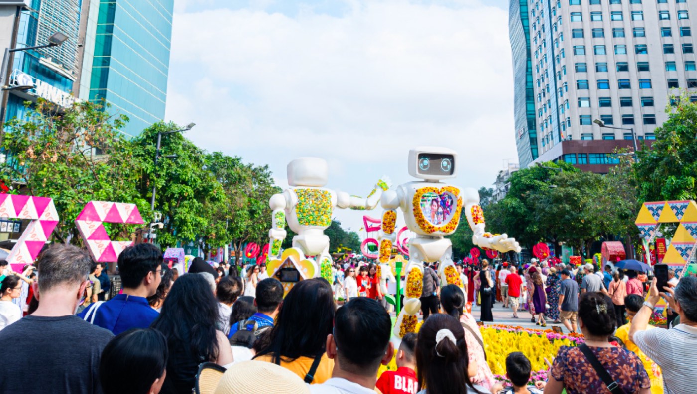 Two flower-covered robots on Nguyen Hue Walking Street, surrounded by a crowd